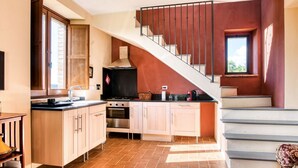Una cucina con isola centrale, piano cottura, forno e lavello. Si nota una scala con ringhiera in metallo che conduce a un piano superiore.