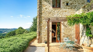 Una casa de piedra con un patio, muebles de exterior y vistas al campo.