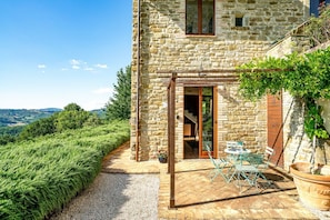 Una casa de piedra con un patio, muebles de exterior y vistas al campo.