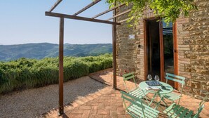 Un edificio in pietra con una pergola, un tavolo con sedie e vista sulle colline.