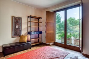 A room with a bench, a bookshelf, a radiator, and a large sliding glass door leading to a garden.