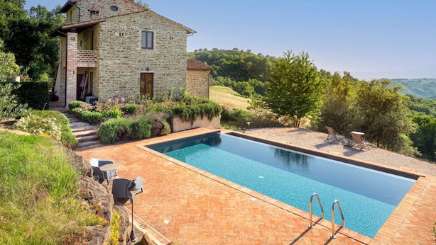 Una casa de piedra con piscina, rodeada de vegetación y colinas.