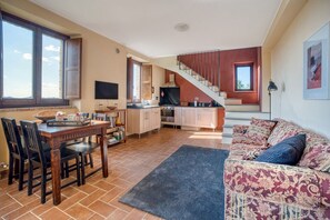 A spacious living area with a dining table, chairs, a sofa, a staircase, and a kitchen in the background.