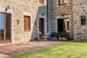 Ein Steinhäuschen mit Terrasse, Sitzgelegenheiten im Freien und einem kleinen Garten.