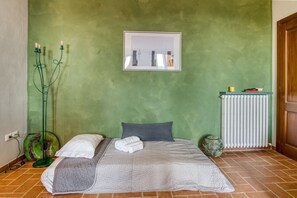 Ein Schlafzimmer mit grüner Wand, einem Bett mit weißer und grauer Bettwäsche, einem Heizkörper und einer grünen Stehlampe.