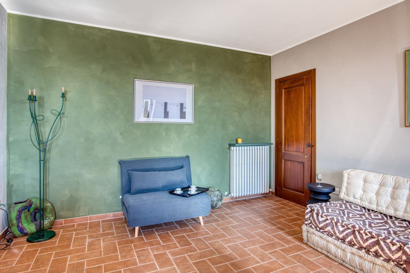Una habitación con un sofá azul, una cama con estampado, un radiador y un cuadro en la pared.