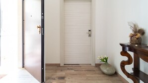 A hallway with a closed door, a small vase with flowers, and a wooden console table. - GuestHost - Borgata Santa Lucia Cozy Apartment! (Siracusa)