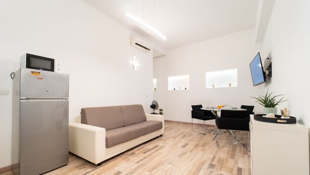 A modern kitchen with a refrigerator, microwave, and a dining area with a table and chairs. - GuestHost - Borgata Santa Lucia Cozy Apartment! (Siracusa)