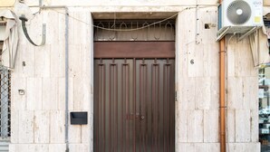 A closed metal gate with a small rectangular window, a wall-mounted air conditioning unit, and a utility pipe. - GuestHost - Borgata Santa Lucia Cozy Apartment! (Siracusa)