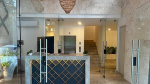 Un área de recepción con mostrador de mármol, separadores de vidrio y una escalera que conduce a un piso superior.