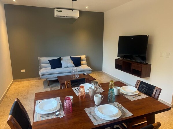 A dining area with a wooden table set for four, a sofa, and a TV mounted on the wall.