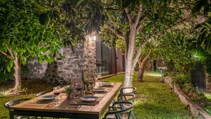 Un espace de restauration en plein air avec une table dressée pour quatre personnes, entouré d’une végétation luxuriante et d’un mur en pierre.