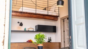 Un coin repas avec une table ronde, des chaises en osier, une plante en pot et une suspension noire.