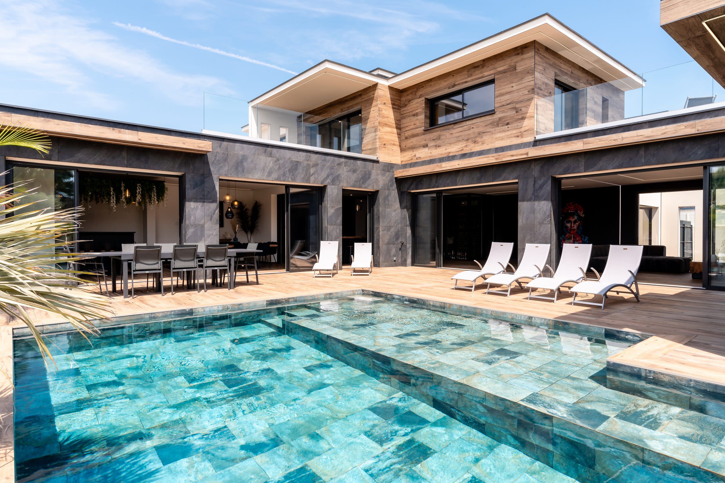 Un espace piscine moderne doté d’une piscine à eau claire, de chaises longues et d’un coin repas avec une table et des chaises.