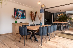 A modern dining area with a wooden table and black upholstered chairs, a colorful abstract painting on the wall, and a kitchen visible in the background.