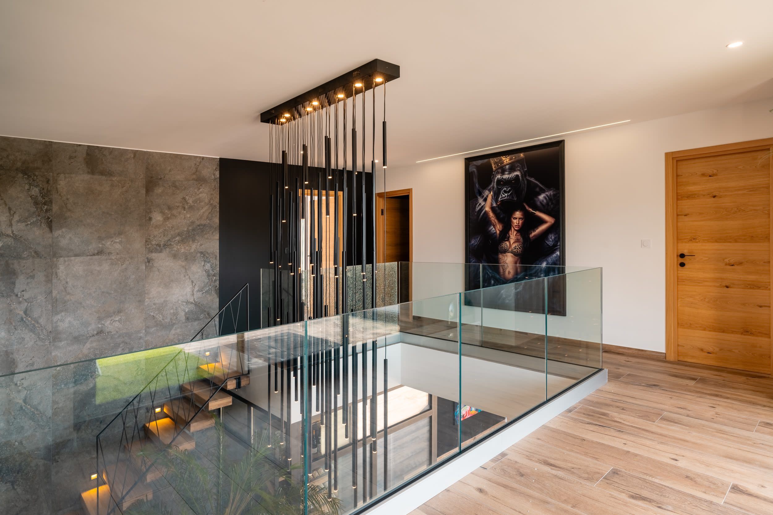 A modern interior with a glass railing, a staircase, and a large framed artwork on the wall.