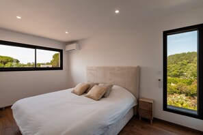 A bedroom with a large bed, a window, and an air conditioning unit.