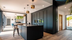 Une cuisine moderne dotée d’un îlot central, de luminaires suspendus et offrant une vue sur l’extérieur.