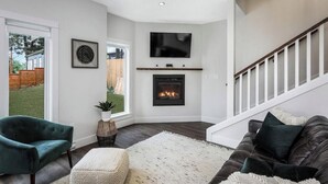 A living room with a fireplace, a television mounted above it, and a staircase leading to another level.
