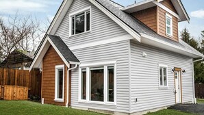 A two-story house with a gabled roof, white siding, and a wooden deck.