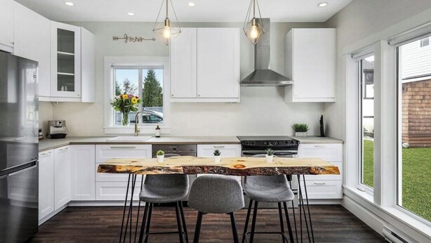 A modern kitchen with white cabinetry, a central island with stools, pendant lighting, and a view of the outdoors.