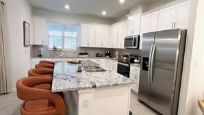 Una cocina moderna con armarios blancos, un refrigerador de acero inoxidable, microondas integrado y encimera de mármol.