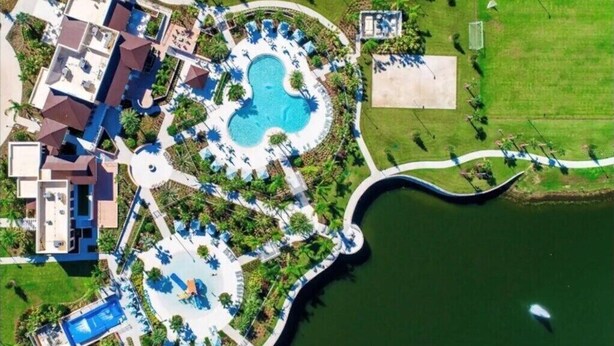 Vista aérea de un resort con piscina central, varias edificaciones para huéspedes y áreas ajardinadas circundantes.