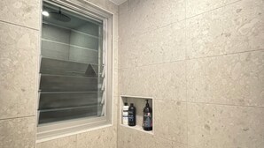 A small, tiled shower room with a window and a shelf holding toiletries. - Luxury new 2 bedrm with ensuites, scenic views & outdoor bath close to winery 🍇 (Mount Alford)