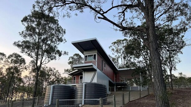 A modern building with a slanted roof, large cylindrical tanks, and a fenced area with trees. - Luxury new 2 bedrm with ensuites, scenic views & outdoor bath close to winery 🍇 (Mount Alford)
