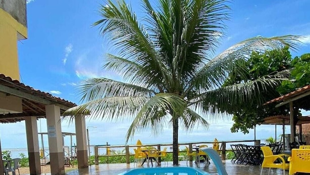 Une piscine avec un palmier, des chaises jaunes et une vue sur l’océan.