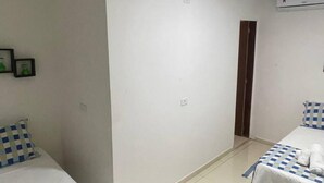Une chambre d’hôtel avec deux lits, un sol carrelé de carreaux blancs et une porte donnant sur une autre pièce.