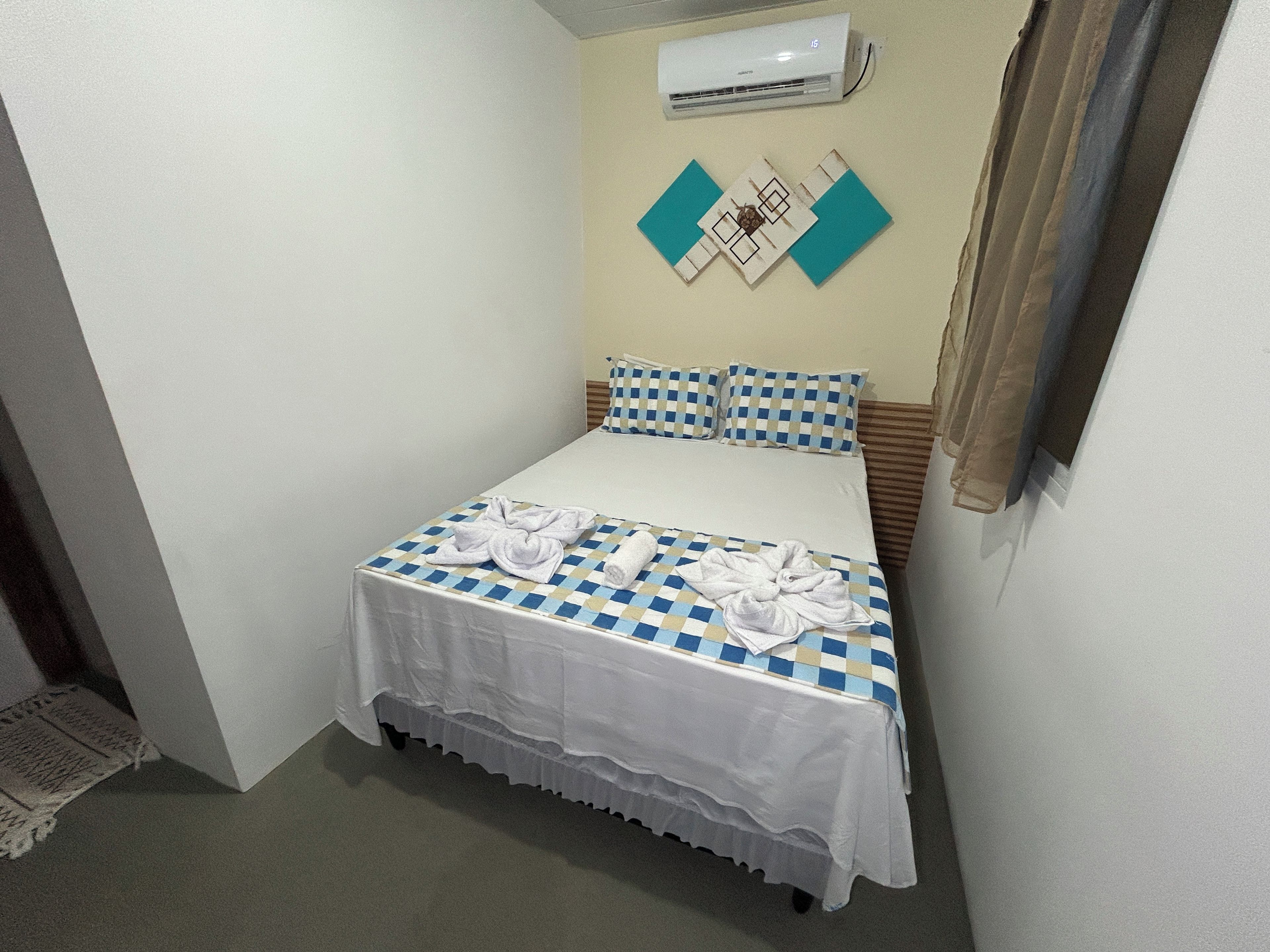 Una habitación pequeña con cama individual, una colcha a cuadros, falda para cama blanca y aire acondicionado de pared.
