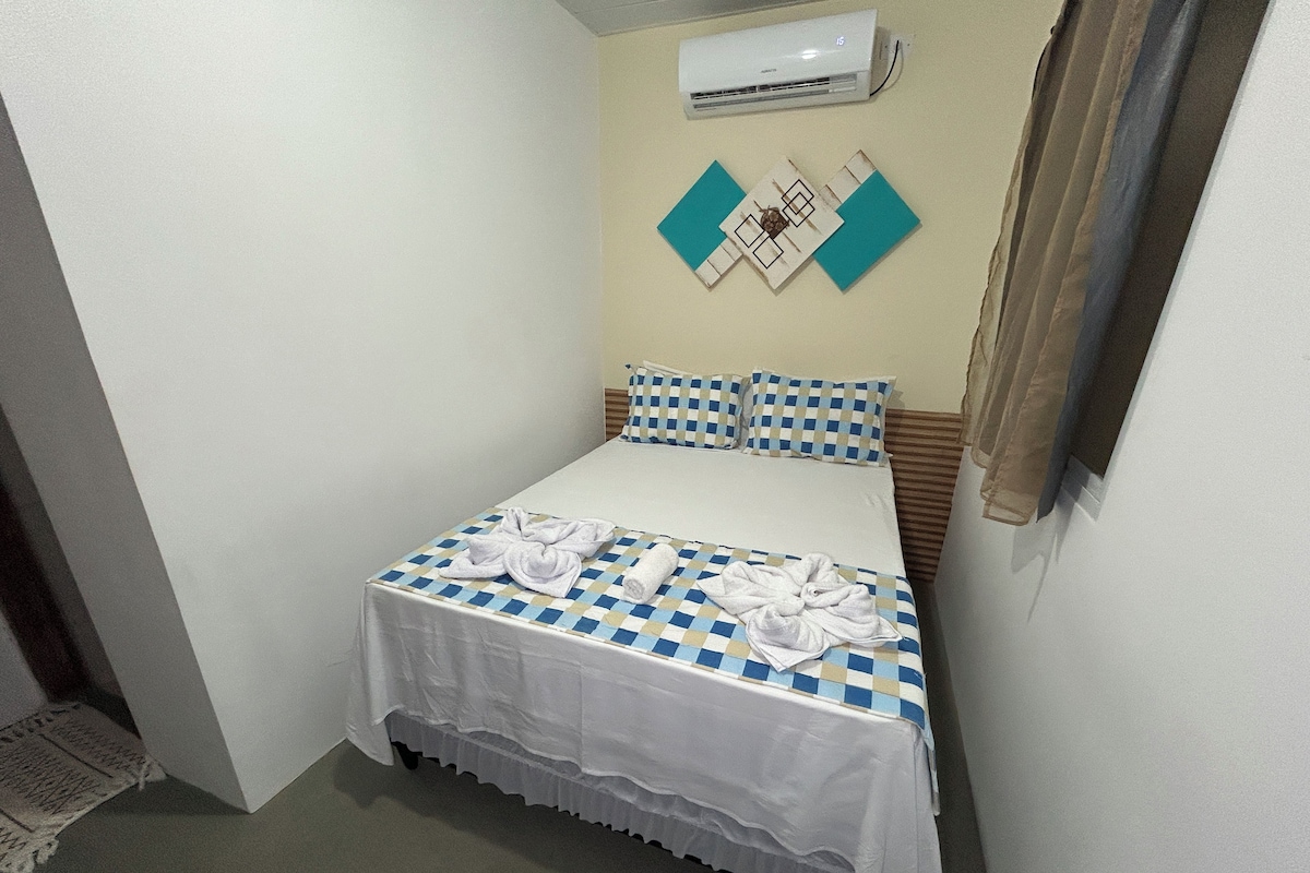 Una camera piccola con un letto singolo, una coperta a quadri, un copriletto bianco e un condizionatore d'aria a parete.