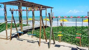 Une plage avec une structure en bois, des balançoires et des parasols.