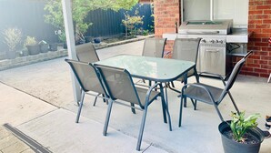 Een terras buiten met een tafel, stoelen, een barbecue en potplanten.