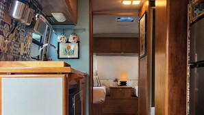 Interior compacto de uma RV com cozinha compacta, espaço para refeições e área de dormir.