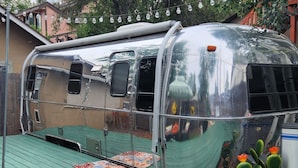 Uma caravana antiga com teto verde, uma pequena área de deck e uma planta de cacto.