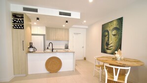 A modern kitchen with a central island, white cabinetry, and a dining area with a round table and white chairs. - UNIT 20707 1bed Unit (Sunshine Coast)