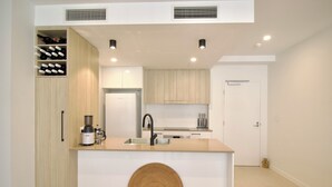 A modern kitchen with a central island, built-in wine storage, and a large woven mat. - UNIT 20707 1bed Unit (Sunshine Coast)