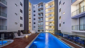 A modern hotel with a central swimming pool, multiple balconies, and a wooden deck area. - UNIT 20707 1bed Unit (Sunshine Coast)