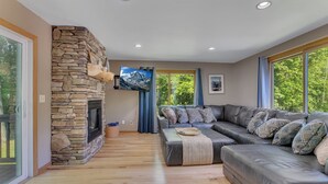 A modern living room with a stone fireplace, a large sectional sofa, and a flat-screen TV mounted on the wall.