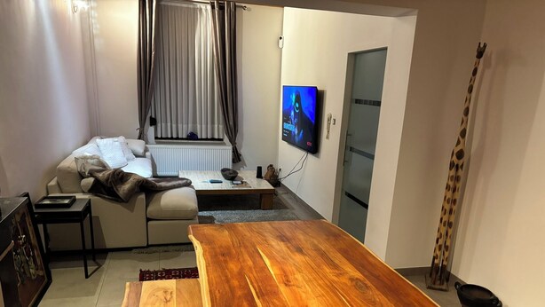 A modern living room with a wooden coffee table, a sofa, a TV mounted on the wall, and a giraffe decoration. - MAISON UNIFAMILIALE (Brussels)