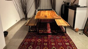 A dining area with a wooden table and benches, a patterned rug, a vase with branches, and a small cabinet with decorative items. - MAISON UNIFAMILIALE (Brussels)