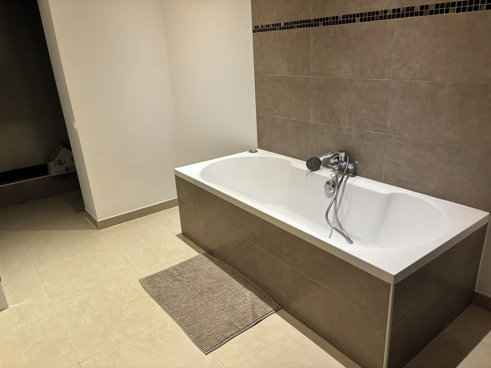 Een moderne badkamer met een vrijstaand bad, een douchekop en een klein vloerkleed.