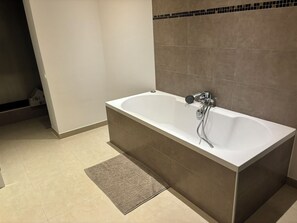 Een moderne badkamer met een vrijstaand bad, een douchekop en een klein vloerkleed.