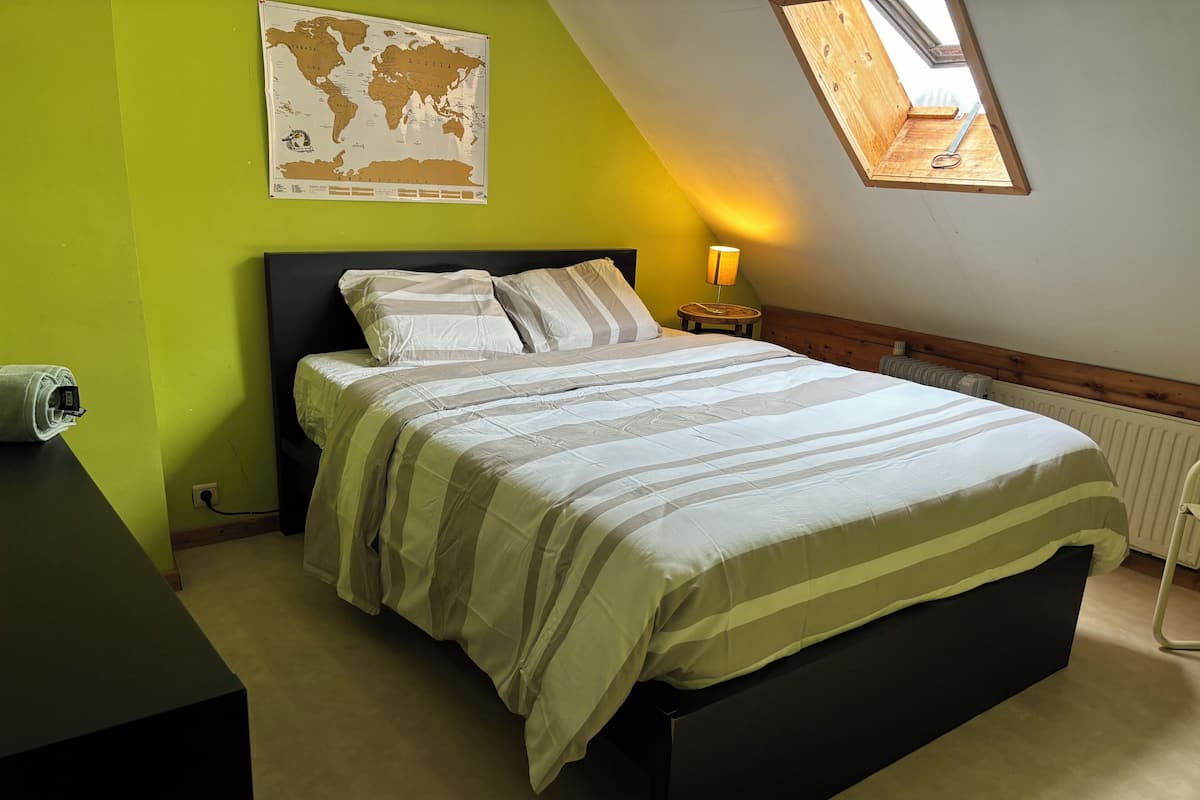 A bedroom with a bed, a world map on the wall, a lamp, and a skylight.