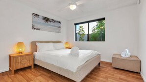 A bedroom with a bed, two bedside lamps, a window with a view of greenery, a small bedside table, and a wall-mounted artwork. - Lovely 2 bedroom ground floor apartment in Noosa Heads with generous private courtyard. (Noosa Heads)