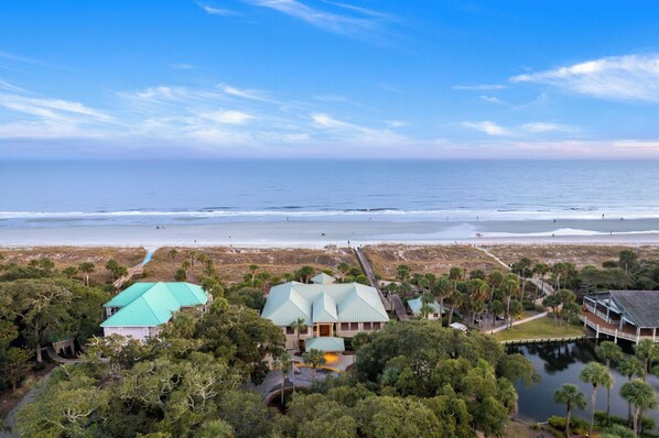 A coastal property with a large house featuring a green roof, surrounded by dense vegetation and a beach in the background. - 253 Evian @ Shipyard | Beach, Golf, Tennis & Pool | Gem on the Greens! (Hilton Head Island)