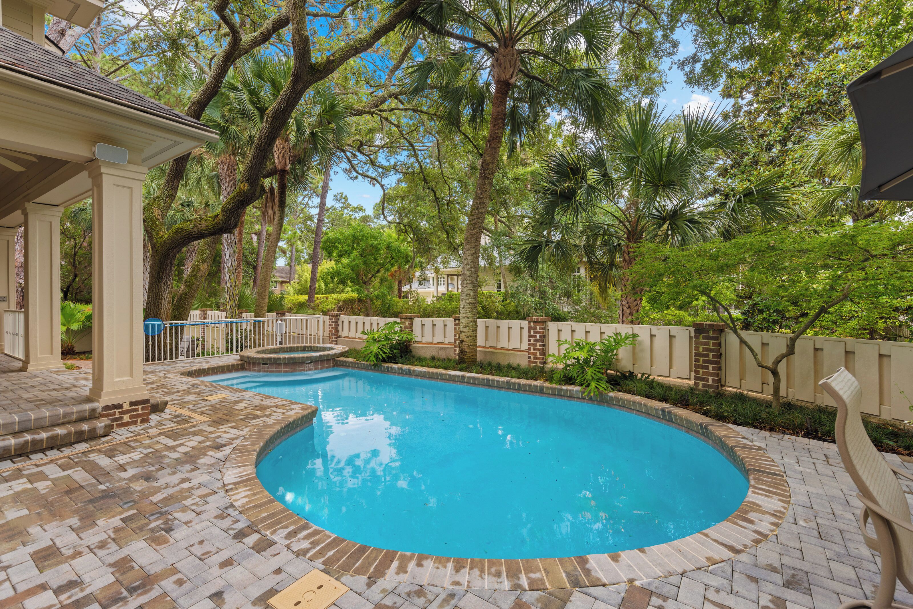 A swimming pool with a brick deck, surrounded by palm trees and a fence.