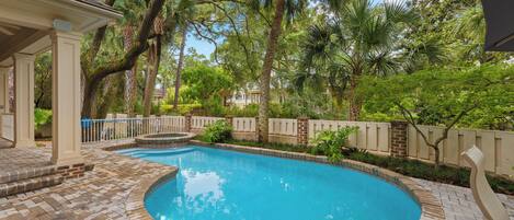 A swimming pool with a brick deck, surrounded by palm trees and a fence.